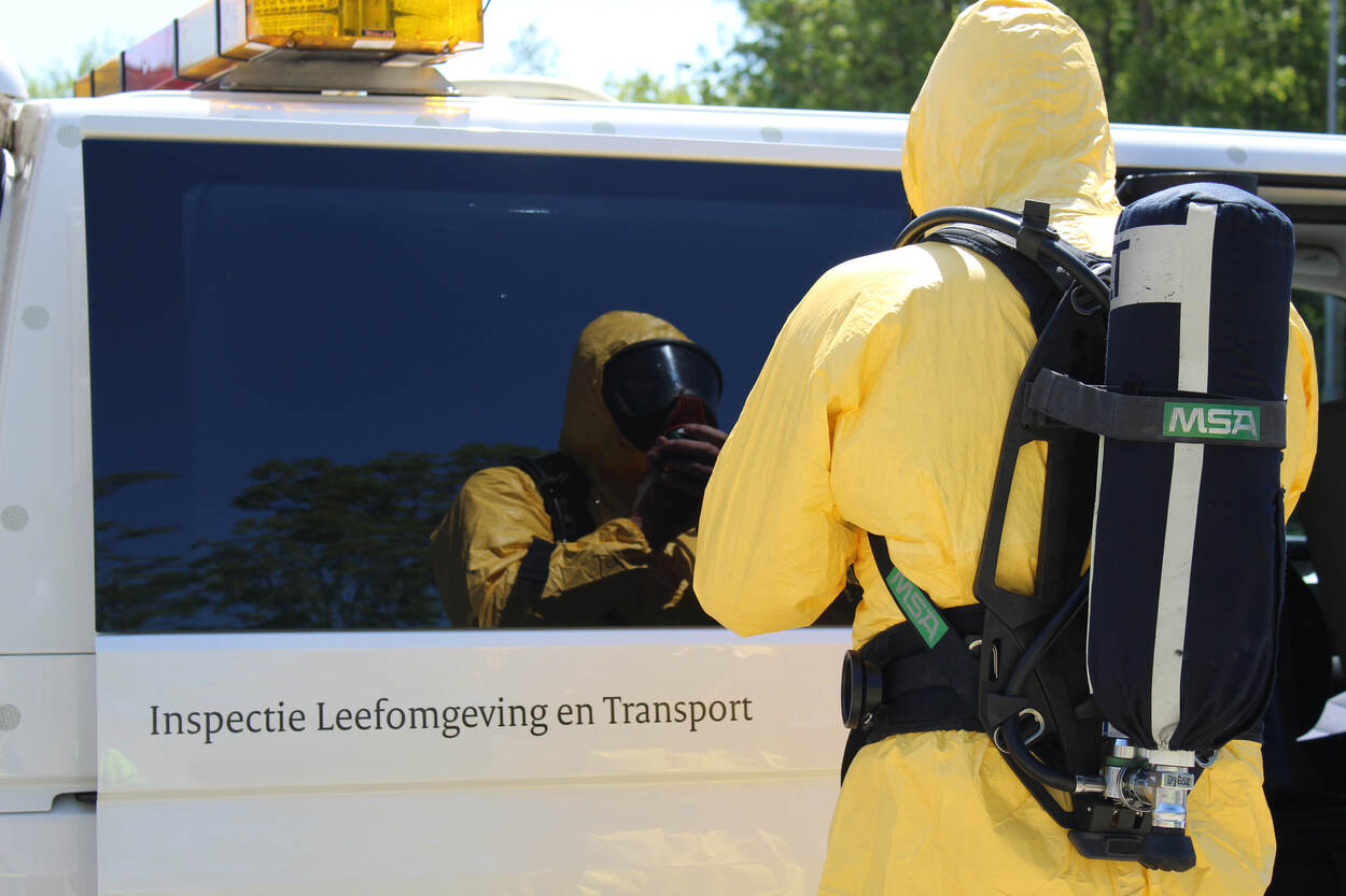 Een inspecteur van het meet- en monstername team staat in beschermende kleding naast een ILT-bus.