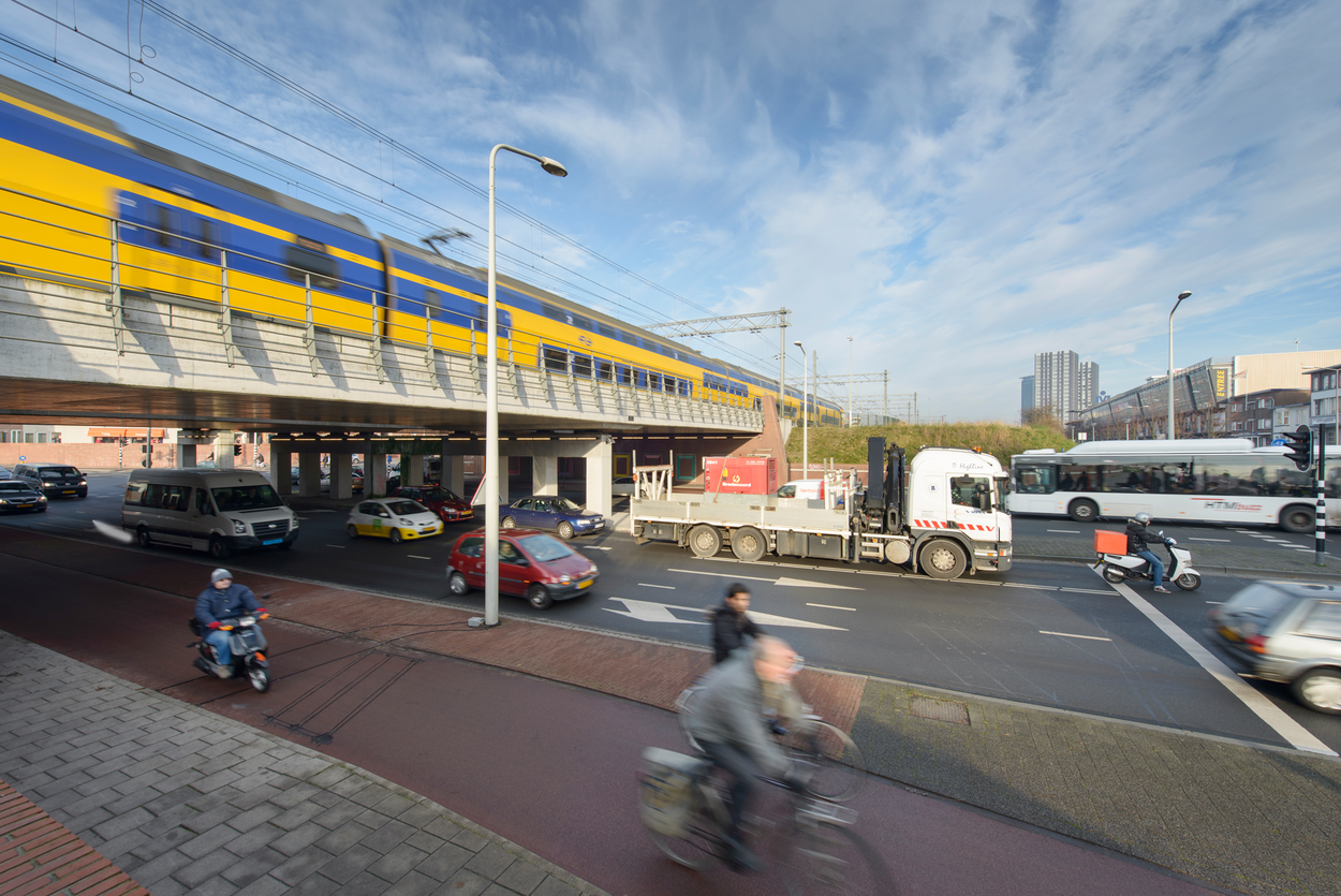 Over een viaduct rijdt een trein. Onder het viaduct loopt een drukke weg. Hier rijden onder andere fietsers, vrachtwagens en auto's.