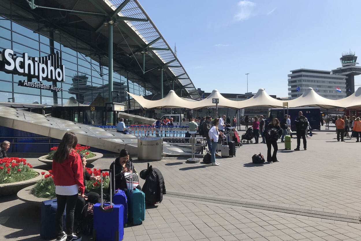 De entree bij luchthaven Schiphol. Diverse passagiers lopen de luchthaven in en uit.