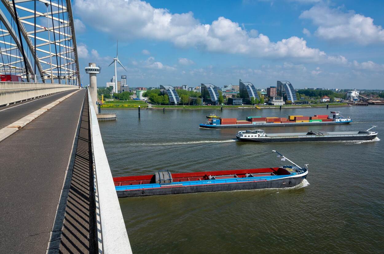 Enkele binnenvaartschepen varen over een rivier.