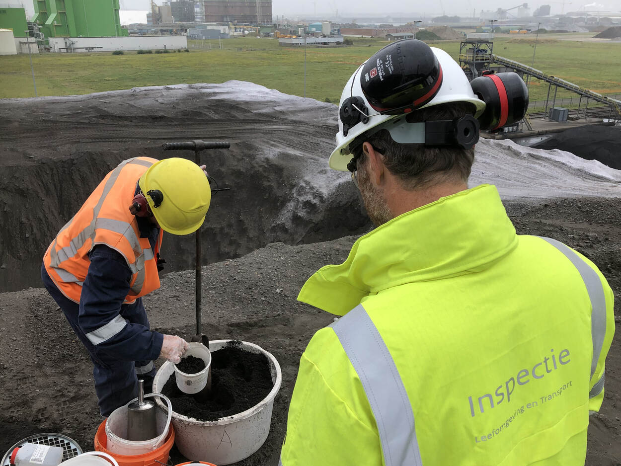 Een inspecteur kijkt toe hoe een monster wordt genomen van een berg termisch gereinigde grond.
