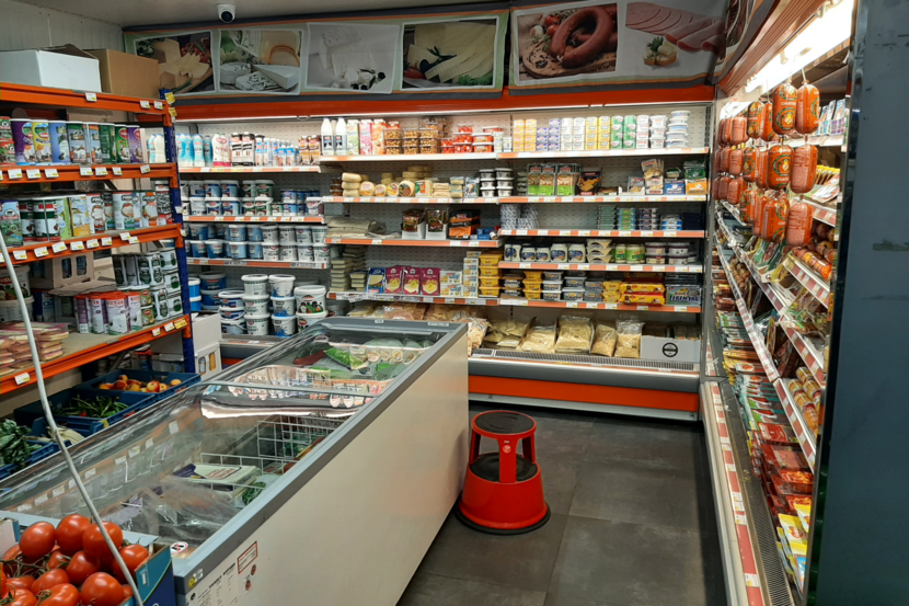 Kleine buurtsupermarkt met open koelinstallaties voor etenswaren.
