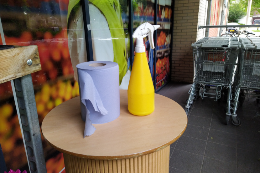Tafeltje met desinfecteer-spray en keukenrol bij de ingang van een winkel in coronatijd.