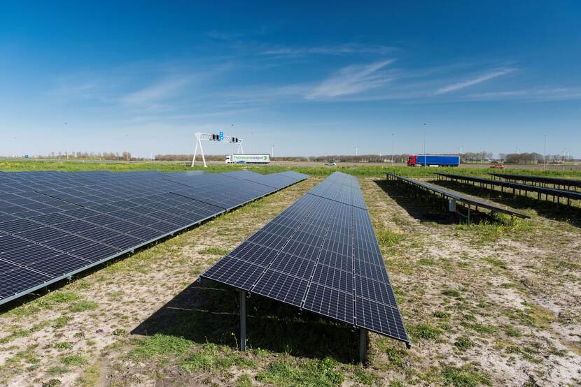 Een veld zonnepanelen langs een snelweg. In de verte rijden vrachtwagens.