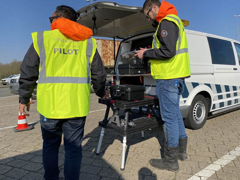 Twee inspecteurs in gele hesjes staan naast een inspectie bus. Ze bedienen een drone.