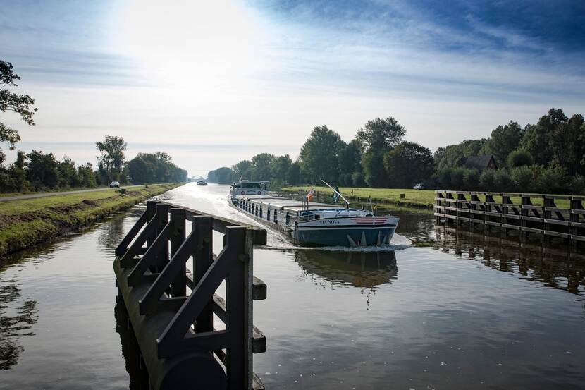 Binnenvaartschip nadert de ingang van een geopende brug in een kanaal.