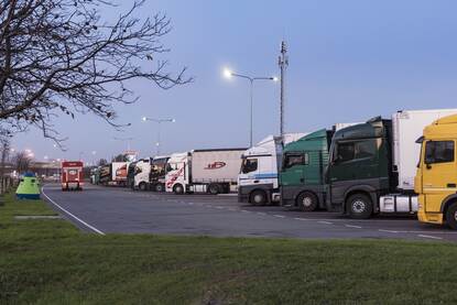 Grote parkeerplaats langs snelweg waar rijen vrachtwagencombinaties staan om te overnachten.