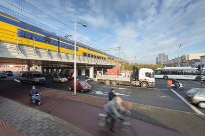 Over een viaduct rijdt een trein. Onder het viaduct loopt een drukke weg. Hier rijden onder andere fietsers, vrachtwagens en auto's.