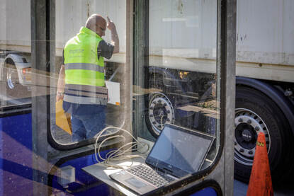 Een vrachtwagen staat op een weegbrug. Een inspecteur geeft de chauffeur van de vrachtwagen aanwijzingen waar hij moet staan.