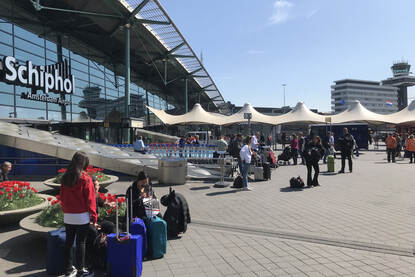 De entree bij luchthaven Schiphol. Diverse passagiers lopen de luchthaven in en uit.