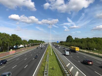 Uitzicht over de snelweg A12 vanaf een loopbrug. Auto's en vrachtwagens rijden voorbij.