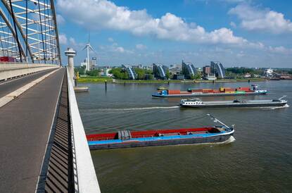 Enkele binnenvaartschepen varen over een rivier.