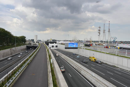 Auto's rijden over een snelweg. Aan de rechterkant van de snelweg ligt een haven met schepen.