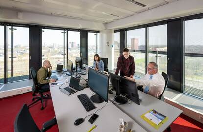 In een kantoorpand zitten mensen achter een bureau en zijn aan het werk.