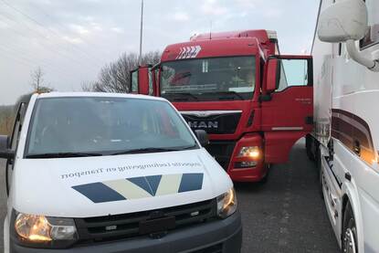 Dienstbusje van inspecteurs bij vrachtwagens op parkeerplaats voor transportcontroles.