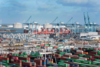 Een havengebied vanuit de lucht. Op de voorgrond staan zeecontainers. Op de achtergrond vaart een zeeschip.